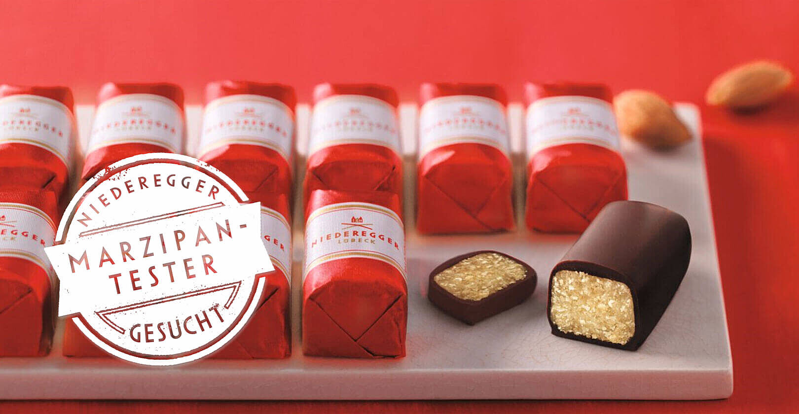 Marzipan Klassiker der Firma Niederegger in zwei Reihen aufgereiht, eingepackt in rote Wickler mit einer weißen Banderole. Auf der rechten Seite ist ein Klassiker angeschnitten worden.